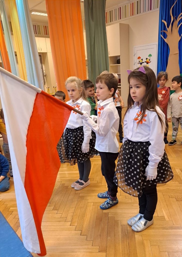 troje, na galowo ubranych dzieci trzyma flagę Polski